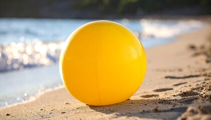 Obraz premium Yellow beach ball resting on a sandy shore near gentle ocean waves
