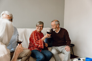 Man and woman smiling and clinking glasses while sitting on a sofa next to a man and a woman