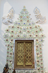 Wooden door entrance on white concrete wall of the church in Wat Phra That Cho Hae.