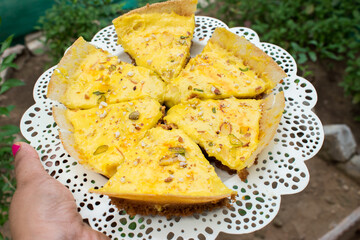 hand holding plate full of ghewar topped with malai. It is a rich winter dessert of India