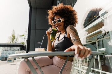 A woman drinks through a straw from a glass while smiling and sitting at the table