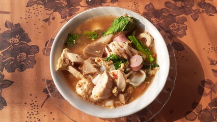 A bowl of Seblak on the table. A typical West Javanese dish. Made with crackers, galangal, garlic, eggs, vegetables, meatballs, sausage, and chicken feet. Wet Seblak. Soup Seblak.