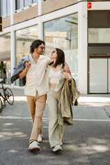 A man and a woman are hugging and holding outerwear while smiling and looking at each other on a walk