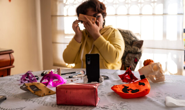 A person is seated at a table adorned with makeup, masks, and Halloween decor, adjusting their preparation amidst a well-lit interior setting.