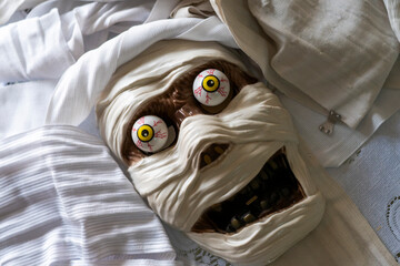 High angle view of spooky mummy head mask and costume featuring exaggerated cartoonish eyes and bandages, ideal for Halloween celebrations or themed events.