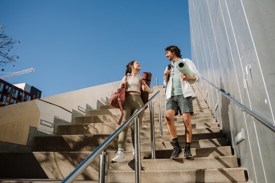 A man and a woman are smiling and walking down the stairs while holding mats