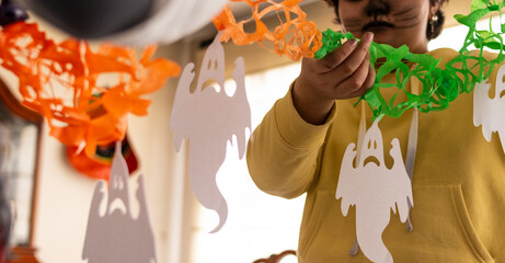 A close-up of woman with painted face holding vibrant Halloween-themed paper decorations, featuring ghost designs in bright colors, reflecting the festive spirit and creativity of the holiday season.