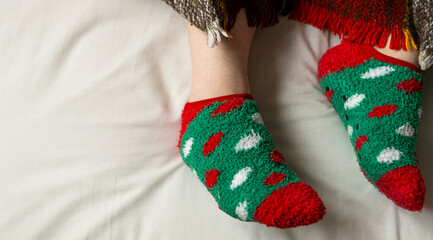Festive themed socks featuring green and red patterns, with copy space on bed, perfectly capturing the warmth and coziness of the holiday season.