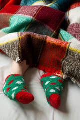 Vertical shoot of blanket covering feet wearing festive themed socks featuring green and red patterns, with copy space on blanket, perfectly capturing the warmth and coziness of the holiday season.