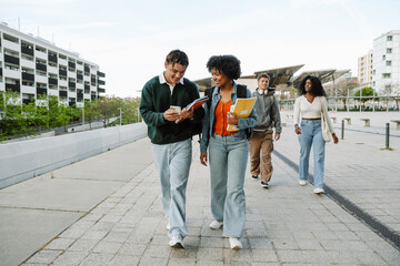 Male and female students smiling and looking at the phone he is holding while they are holding notebooks