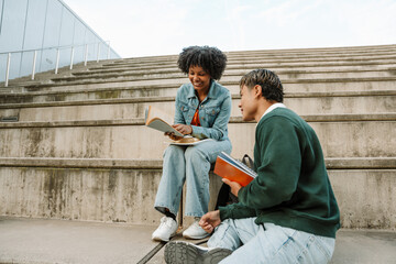 Male and female students sitting on bleachers looking at the book she is holding and smiling