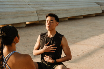 A man placed his hands on his chest and stomach while sitting with his eyes closed opposite a woman