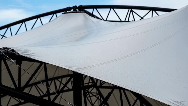 Closeup details of the fabric membrane stretching across steel framework during concert roof deployment highlighting texture and tensile architecture.
