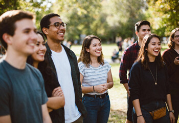 Fototapeta premium Happy young adults smiling and socializing outdoors in park during sunny day, diverse group of friends enjoying community event or gathering in relaxed atmosphere