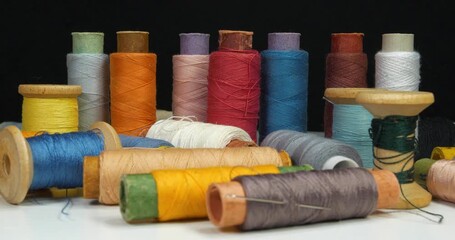 Beautiful multi-colored spools of thread lie on white table rotates on black background - Powered by Adobe