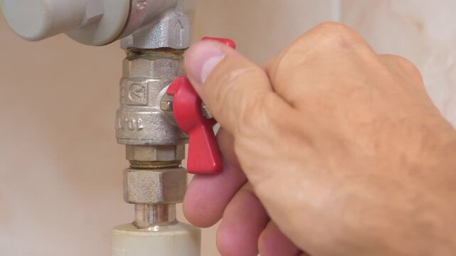 Red valve on cold water pipe to boiler for heating. Boiler heats water from cold water supply system. Man turns red valve and cut off the cold water supply to boiler