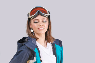Young caucasian female skier in blue jacket with ski goggles relaxing on gray background.