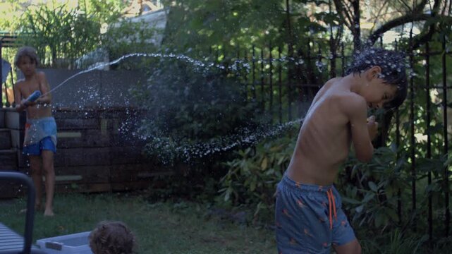 Two boys battling with water blasters in backyard garden, playful chase and splashes on hot summer day, joyful childhood fun and laughter captured in slow motion