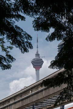 Kuala Lumpur Tower Rising Against Cloudy Sky with Tree in Foreground