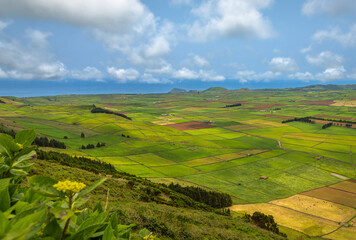 Panoramic view of the colorful agricultural fields from Serra do Cume lookout on Terceira Island, Azores, Portugal. Lush green, yellow, and brown farmlands form a scenic patchwork landscape 