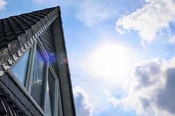 Sunlight illuminating a slate roof with clouds and blue sky