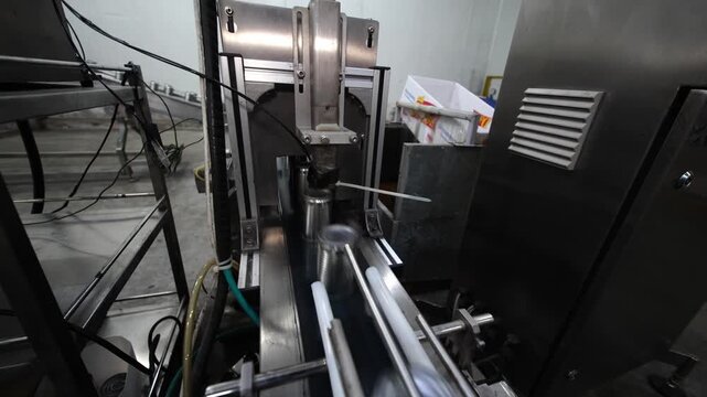 Several metal cans are lined up on a conveyor in a production facility. Workers in the background monitor the machinery's operation, ensuring a smooth flow of the manufacturing process.