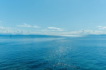 Sparkling blue sea under a bright sky with distant mountains and a small sailboat on the horizon