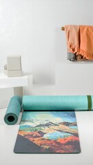 Teal yoga mat with mountain print, rolled and unrolled, on white backdrop with clothing