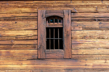 Small barred window in rustic horizontal log wall close‑up
