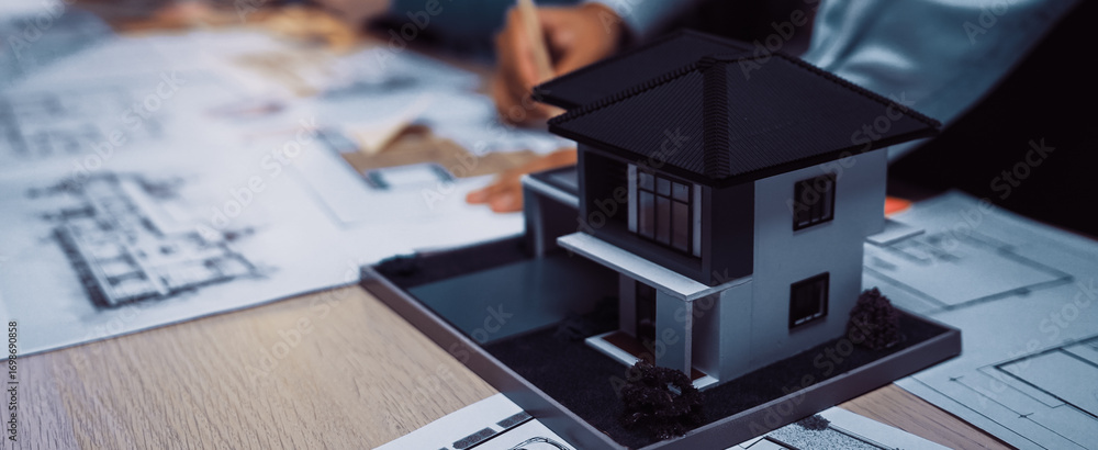 Poster a detailed view of a modern house model placed on a table surrounded by architectural blueprints, sh