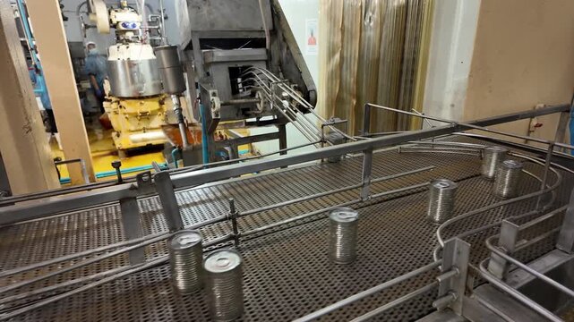 Automated Food Production Line: Cans move along a conveyor belt in an automated food processing plant, showcasing a modern industrial environment focused on efficiency and mass production.