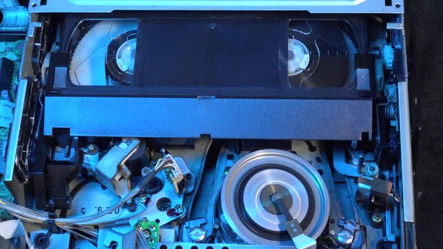 Close-up View of a VCR VHS player with Cassette Tape Inserted in the player with detail on the exposed head drum - LOAD, REW and EJECT movements with colored ligh effects