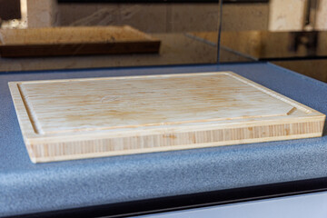 Large wooden cutting board with juice groove placed on modern gray kitchen countertop in natural indoor light