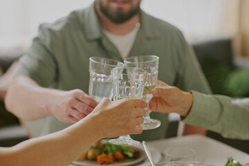 Three Caucasian adults clinking glasses during meal, hands and arms visible, celebrating or making toast at dining table, food and drinks on table, focus on gesture and interaction