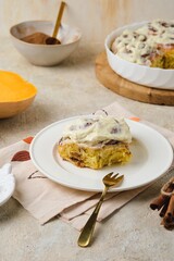 Step by step cooking pumpkin cinnabons on light concrete background. Ready bun with cream on white ceramic plate.