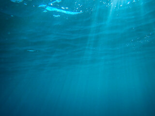 Dark blue ocean surface seen from underwater. Abstract waves underwater and rays of sunlight shining through, Sun light rays undersea deep, Underwater background with sea bottom, Mediterranean sea.