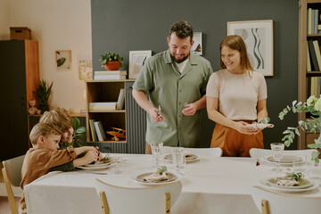 Caucasian middle aged man and woman standing beside dining table preparing meal while two Caucasian...