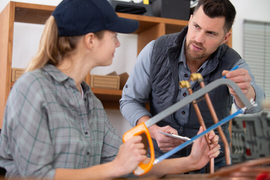 tradeswoman cutting copper pipe with hacksaw