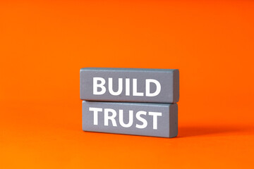 Build Trust written on gray wooden blocks. A symbol of trust in life and business. Conceptual words. Nurturing relationships and good collaboration. Beautiful orange background, copy space.