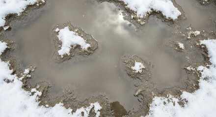Muddy Water Puddle Surrounded by Melting White Snow on a Winter Day