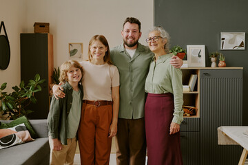Caucasian boy, young adult woman, man, senior Caucasian woman standing together smiling in modern living room, family members posing for group photo