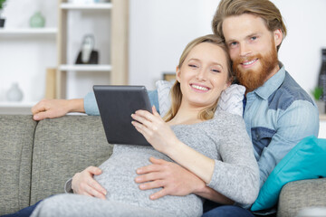 Fototapeta premium attractive happy young man and pregnant woman holding digital tablet