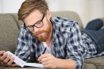 man layed on the sofa writing in a notebook
