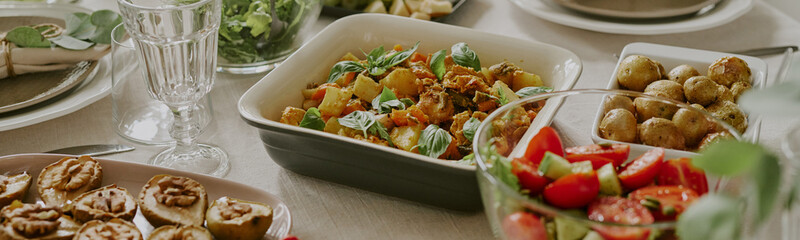 Website banner of assorted vegetable dishes and salads arranged on dining table, showcasing fresh ingredients in serving bowls and plates
