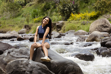 Joyful Woman Sitting on a Rock in a Flowing Rive