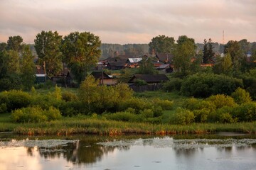 Beautiful lake in summer. Lush greenery, houses in the background, clouds, reflection.