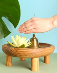 A hand gently rings a small bell over a lotus flower on a wooden tray