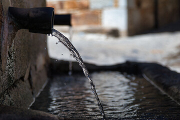 Clear water flowing from an ancient fountain - A stream of clear water flows from a rusty pipe into a stone trough, creating ripples and small splashes.