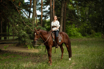 Beautiful young woman in stylish white blouse, black pants and high boots with a horse outdoors