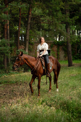 Beautiful young woman in stylish white blouse, black pants and high boots with a horse outdoors